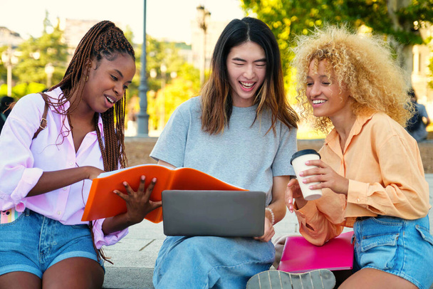 Troje szczęśliwych wielorasowych przyjaciół studiujących z folderem i laptopem w parku. - Zdjęcie, obraz