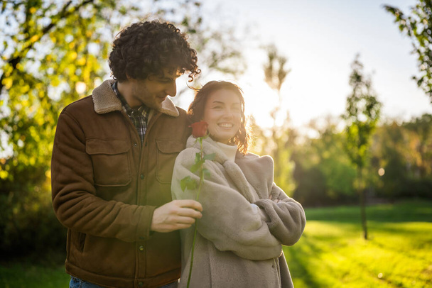Портрет щасливої закоханої пари в парку на заході сонця. Чоловік дає троянду своїй жінці. - Фото, зображення