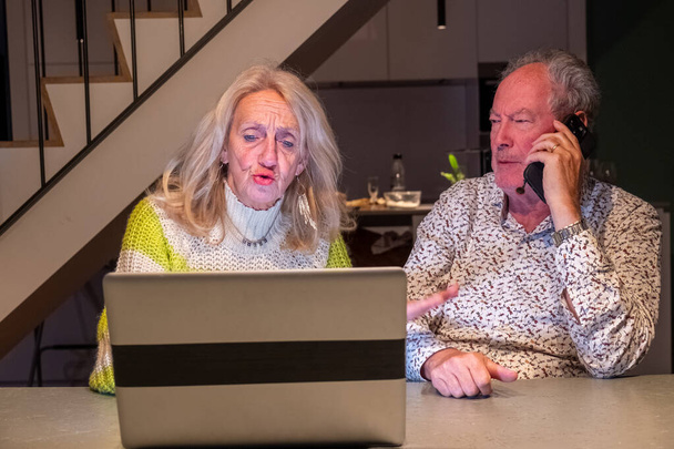 Obrázek zobrazuje starší pár zapojený do něčeho, co se zdá být kooperativním úkolem v domácím kancelářském prostředí. Zdá se, že žena se svou pozorností upřenou na obrazovku notebooku diskutuje - Fotografie, Obrázek
