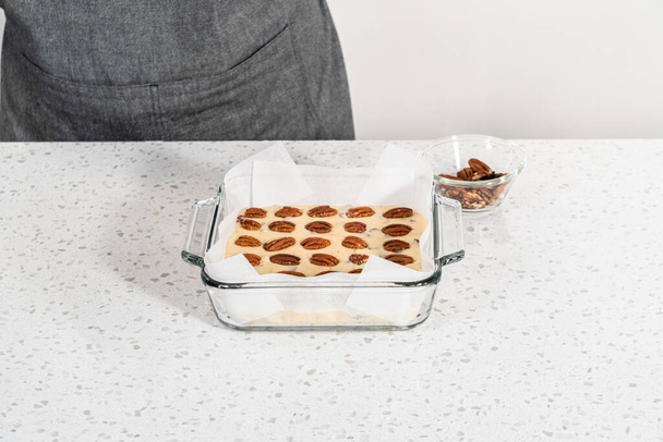 白チョコレートクランベリーのピーカン・ファッジを作るために、パーチメント紙で並んだベーキングパンに生地の混合物を注ぐ. - 写真・画像