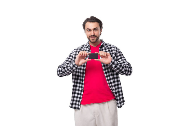 mladý chytrý brunetka kavkazský muž se stylovým účesem a vousy drží bankovní karty mockup izolované na bílém pozadí. - Fotografie, Obrázek
