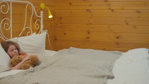 Panning záběr malého chlapce spícího v posteli v dřevěné ložnici, objímající jeho oblíbenou hračku - Záběry, video