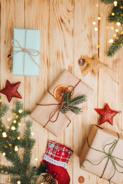 Kerst achtergrond. Cadeaus verpakt in bruin papier met droog oranje en tak van naaldboom op een lichte houten achtergrond. Bovenaanzicht - Foto, afbeelding