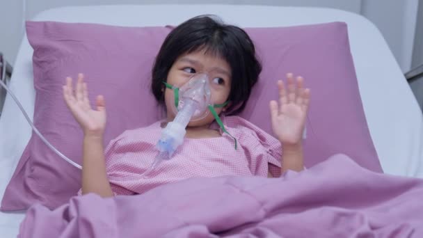 Egy ázsiai kislánynak oxigénmaszkja van, és porlasztón keresztül lélegzik a kórházban. Fogalma hörghurut, légzőszervi és orvosi kezelés, inhalációs orvoslás, köd, egy porlasztó. - Felvétel, videó