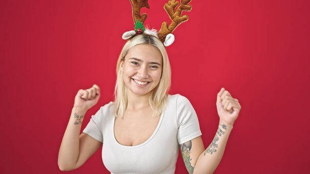 Young beautiful hispanic woman wearing reindeer christmas hat dancing over isolated red background - Foto, imagen