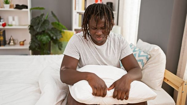 アフリカ系アメリカ人男性は寝室でベッドに座ることを強調しました - 写真・画像