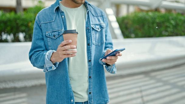 Joven hombre caucásico usando teléfono inteligente beber café en el parque - Foto, imagen