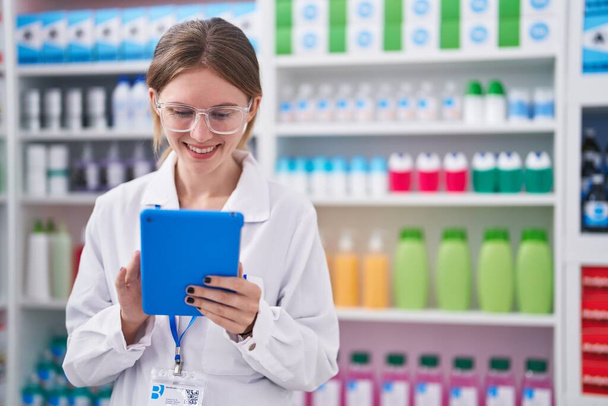 Mladá blondýna žena lékárník úsměv jistý pomocí touchpad v lékárně - Fotografie, Obrázek