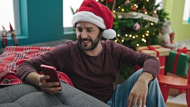 Nuori latino mies käyttää älypuhelin juhlii joulua kotona - Valokuva, kuva