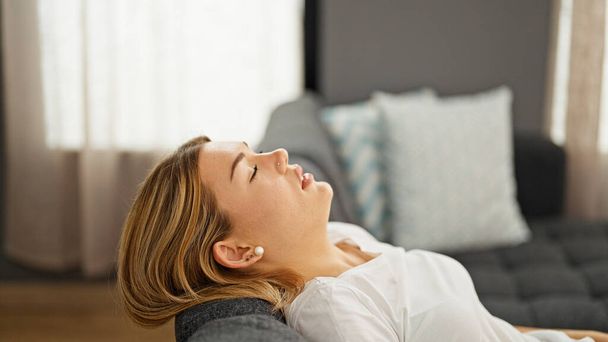Mujer rubia joven relajada en el sofá con expresión cansada en casa - Foto, imagen