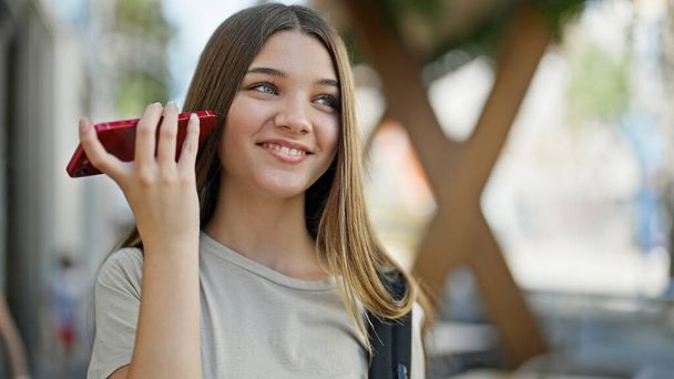 Sırt çantası takan genç ve güzel bir kız sokakta akıllı telefondan sesli mesaj dinliyor. - Fotoğraf, Görsel