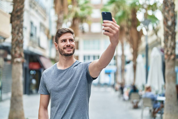 Νεαρός καυκάσιος άνδρας χαμογελά σίγουρος κάνοντας selfie από το smartphone στο δρόμο - Φωτογραφία, εικόνα