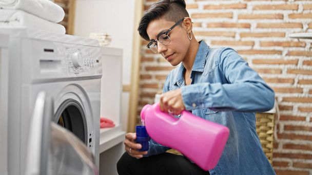 jong mooi latino vrouw wassen kleding gieten wasmiddel in wasruimte - Foto, afbeelding