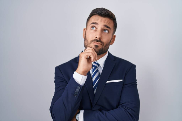 Handsome hispanic man wearing suit and tie with hand on chin thinking about question, pensive expression. smiling with thoughtful face. doubt concept.  - Photo, Image