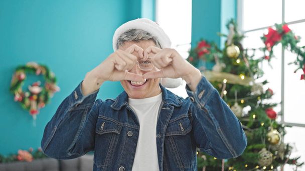 Young caucasian man celebrating christmas doing heart shape with hands at home - Photo, Image