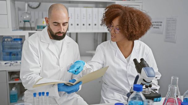 En el corazón de la ciencia, dos científicos resilientes, hablando y leyendo documentos de investigación médica innovadores juntos en el laboratorio. - Foto, imagen