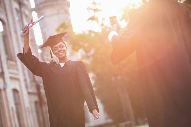 Succesvol afgestudeerden in academische jurken zijn het nemen van foto's met diploma's van elkaar terwijl permanent buitenshuis - Foto, afbeelding