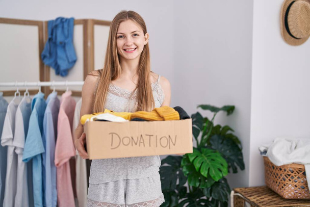 Молодая белая женщина с коробкой пожертвований для благотворительности подмигивает, глядя в камеру с сексуальным выражением лица, веселым и счастливым лицом.  - Фото, изображение
