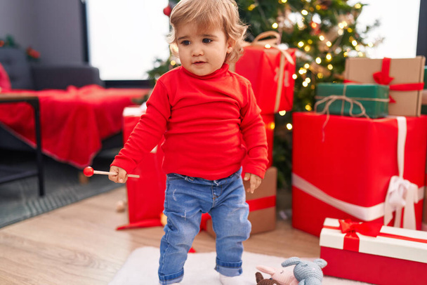 Adorable niño hispano de pie junto al árbol de Navidad en casa - Foto, Imagen
