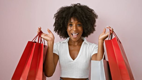 Afroamerykanka uśmiecha się idąc na zakupy torby na odizolowanym różowym tle - Zdjęcie, obraz