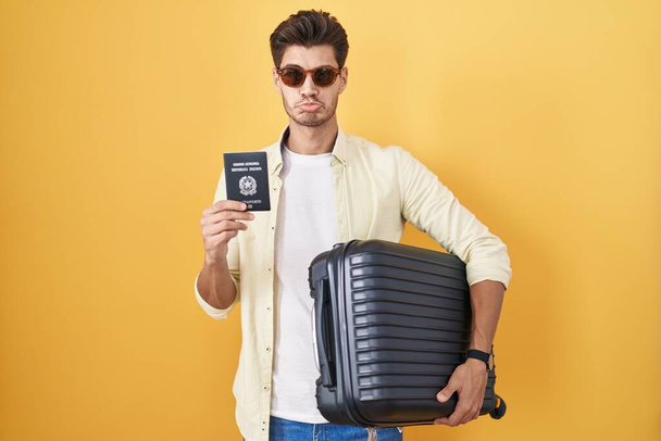 Elinde bavul tutan İspanyol genç adam yaz tatiline çıkıyor. Elinde İtalyan pasaportu var. Depresyonda ve endişe içinde. hüzünlü ifade.  - Fotoğraf, Görsel