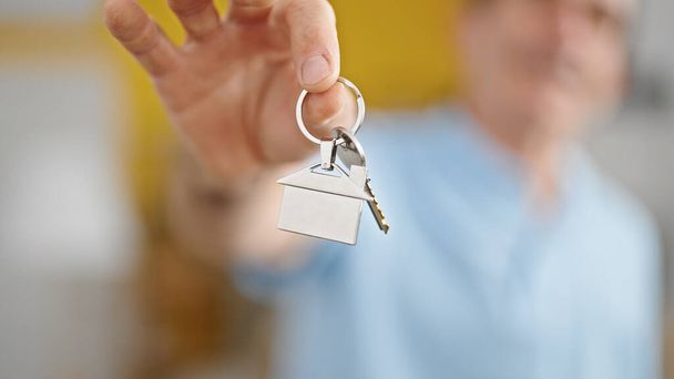 Hombre de mediana edad sonriendo confiado sosteniendo nuevas llaves de la casa en el nuevo hogar - Foto, imagen