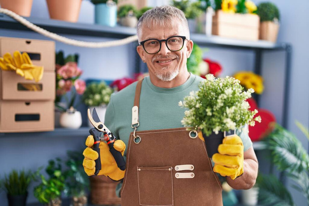 Hombre hispano con el pelo gris trabajando en floristería sonriendo con una sonrisa alegre y fresca en la cara. mostrando dientes.  - Foto, Imagen