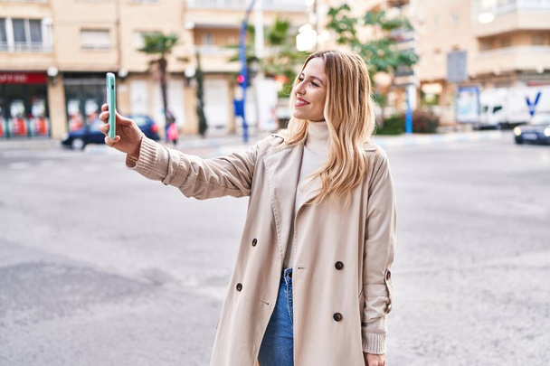 jong blond vrouw glimlachen zelfverzekerd maken selfie door de smartphone op straat - Foto, afbeelding