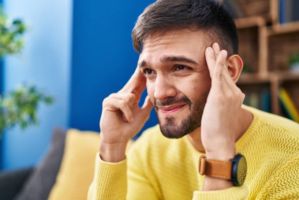 Young hispanic man stressed sitting on sofa at home - Foto, imagen