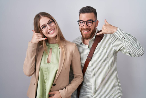 Young couple standing over white background smiling doing phone gesture with hand and fingers like talking on the telephone. communicating concepts.  - Photo, Image