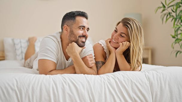 Мужчина и женщина лежат вместе на кровати и улыбаются в спальне. - Фото, изображение
