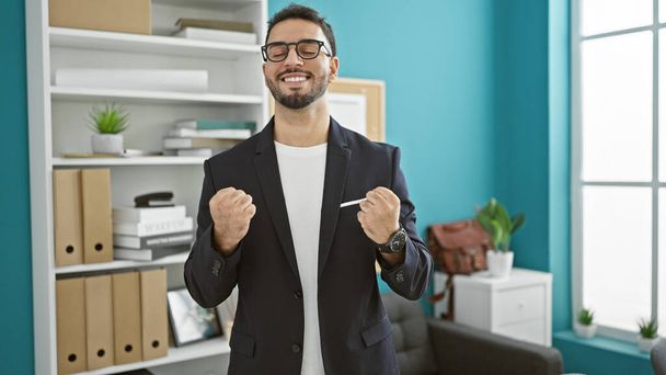 Jonge Arabische man zakenman glimlachend vol vertrouwen vieren op kantoor - Foto, afbeelding