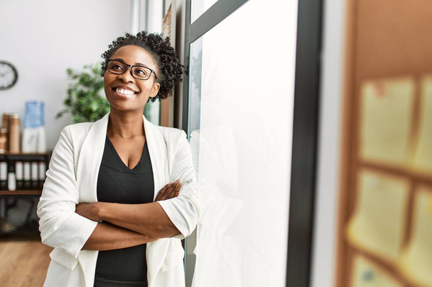 Afrykański amerykański kobieta biznes pracownik uśmiechnięty pewny siebie stojąc z bronią skrzyżowane gest w biurze - Zdjęcie, obraz
