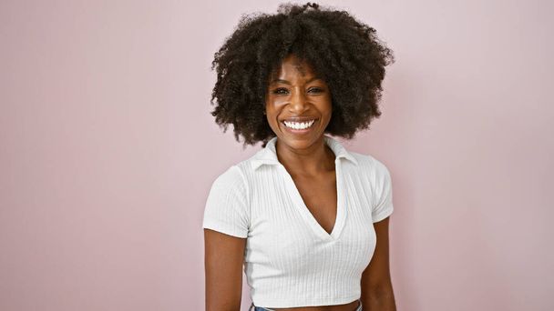 Африканська американська жінка, яка впевнено посміхається, стоячи над ізольованим рожевим фоном. - Фото, зображення