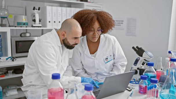 Twee serieuze wetenschappers die samen spreken, die onderzoeksinzichten ontdekken op een laptop in een indoor lab - Foto, afbeelding