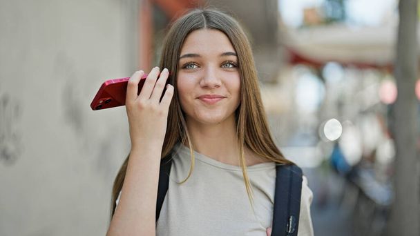 młoda piękna dziewczyna student noszenie plecak słuchanie wiadomości głosowych przez smartfona na ulicy - Zdjęcie, obraz