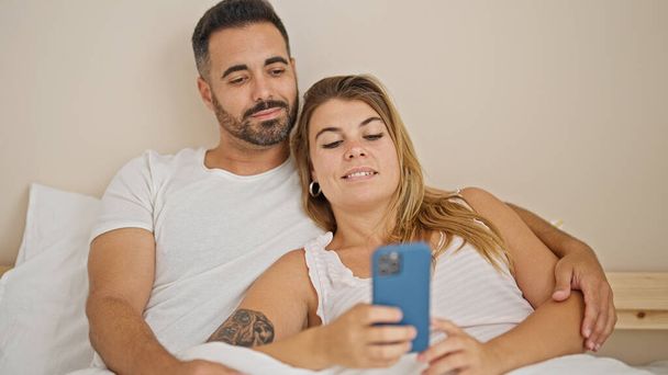 Hombre y mujer pareja acostada en la cama usando un teléfono inteligente abrazándose en el dormitorio - Foto, imagen