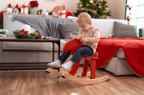 Adorable toddler playing on reindeer rocking by christmas tree at home - Photo, Image