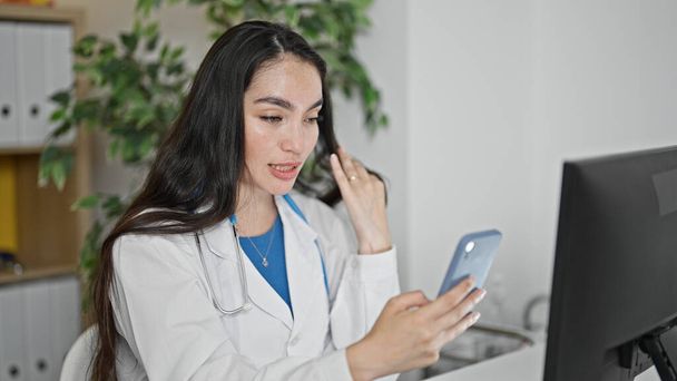 Jeune belle médecin hispanique femme faisant appel vidéo avec smartphone à la clinique - Photo, image