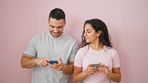 Άνδρας και γυναίκα ζευγάρι χρησιμοποιώντας smartphones χαμογελώντας πάνω από απομονωμένο ροζ φόντο - Φωτογραφία, εικόνα