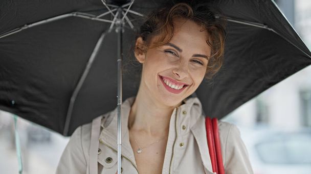 Fiatal nő mosolygós magabiztos gazdaság esernyő az utcán - Fotó, kép