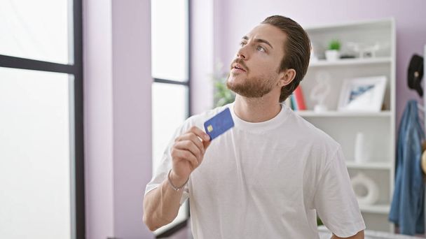 Νεαρός Ισπανός με πιστωτική κάρτα σκέφτεται στο σπίτι - Φωτογραφία, εικόνα