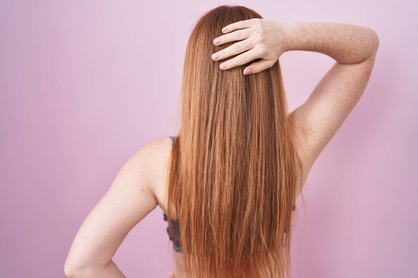 Redhead woman wearing lingerie over pink background backwards thinking about doubt with hand on head  - Photo, Image