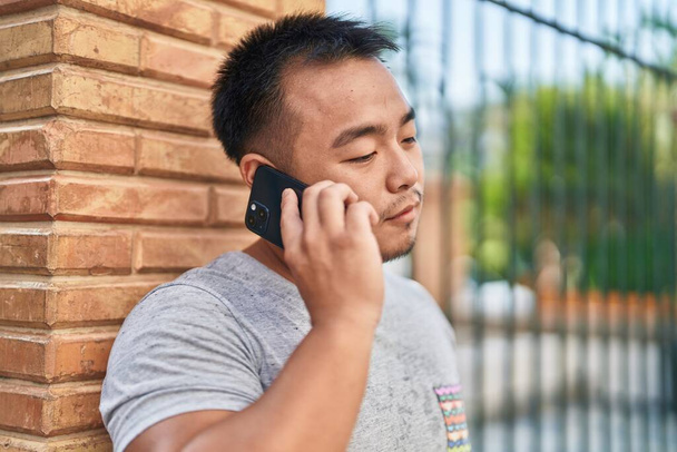 Fiatal kínai férfi beszél az okostelefonon nyugodt kifejezés az utcán - Fotó, kép