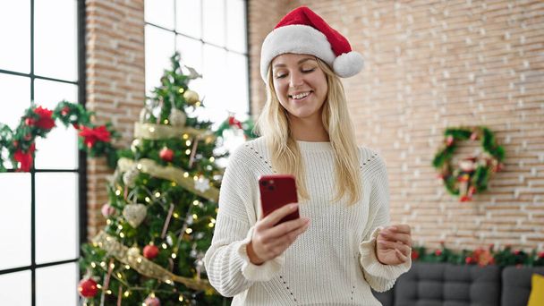 fiatal szőke nő ünnepli karácsonyi okostelefon otthon - Fotó, kép