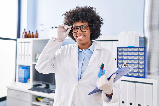 Αφροαμερικανή επιστήμονας χαμογελώντας αυτοπεποίθηση κρατώντας πρόχειρο στο εργαστήριο - Φωτογραφία, εικόνα