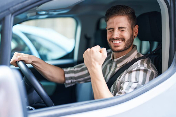 Hispanic man with beard driving car screaming proud, celebrating victory and success very excited with raised arm  - Photo, Image