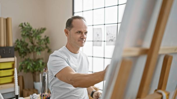 Уверенный в себе мужчина средних лет, улыбающийся художник, искренне любит рисовать в своей студии, направляя свое внутреннее творчество - Фото, изображение