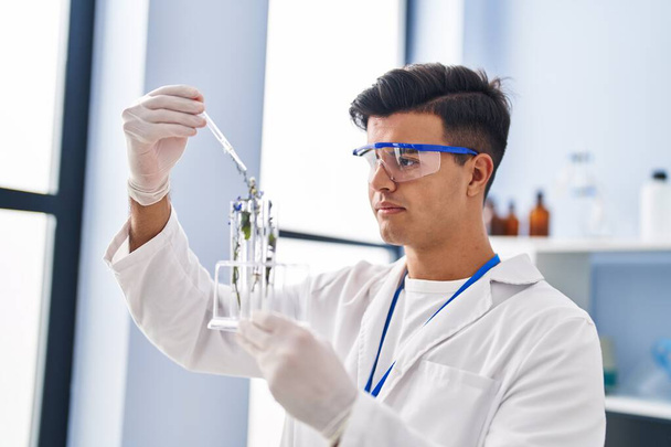Joven científico hispano sosteniendo tubo de ensayo con planta en laboratorio - Foto, imagen