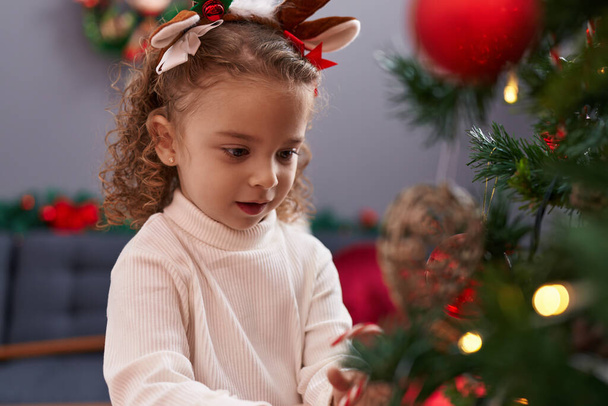 Adorable fille blonde portant des oreilles de renne décorant l'arbre de Noël à la maison - Photo, image